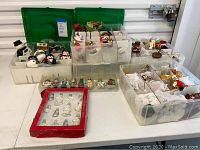 Wide view of multiple clear plastic storage trays containing various Christmas ornaments including snowmen, glass baubles, and figurines.