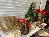 Overall lot display with silk amaryllis flowers, decorated artificial trees, gold wire sleighs, angel tree topper and various Christmas decorations on a table.