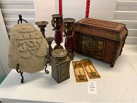 Lot contents including simulated wicker box, two red and gold candlesticks, ceramic jar, stone 'Love' sign, and palm wall art pieces arranged on table