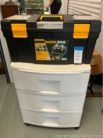 WorkZone black and yellow plastic toolbox on top of white plastic storage drawers with three drawers.