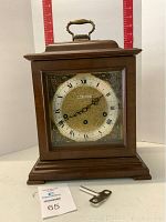 Front view of the Seth Thomas Legacy IV mantel clock showing the wooden case, glass door, clock face with Roman numerals, and brass-tone handle on top.
