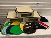 Three beige canvas storage boxes with brown trim and transparent side windows, two similar sized smaller boxes and one larger box, arranged on a table with colorful purse covers and a small black purse in front.