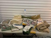 Full view of all assorted linens on white folding table showing stacks of towels, packaged sheets, decorative pillows, and bedding accessories.