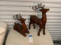 Pair of decorative deer sculptures, one kneeling and one standing, shown on flat surface with unit background.