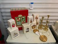 Full lot overview showing Hallmark Keepsake ornaments in original boxes, brass candlesticks, ornament stands, and storage box.