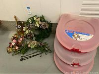 Photo of Christmas wreath, swag, broom decor, wreath storage bins, and metal hangers on floor against wall