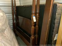 Disassembled wooden four-poster bed frame components leaning against wall