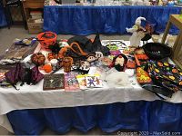 Wide view of a table with assorted Halloween items including costumes, candy bowls, candle holders, CDs, and decorations