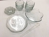 Photo showing stacked small flower-shaped glass bowls and plates, large flower-shaped platter, fruit bowl, and clear serving spoon.