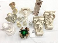 Collection of angel statues, figurines, music box, picture and candles arranged on white surface