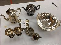 Full view of tea pots, goblets, and other silver-plated items placed on a white surface from an overhead angle.