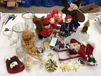 Photo showing a variety of Christmas decorations including glass vases, candle holders, plush teddy bear, fabric Santa figurine, stuffed reindeer, and several small holiday ornaments and figurines.
