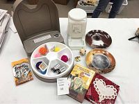 View of Petsafe auto feeder with assorted cat toys, batteries, chicken-flavor treats, cat-themed plates, photo album, novel, and pin arranged on table