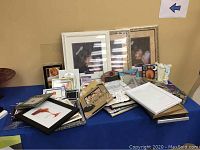 Photo of assorted frames lined on a blue surface, showing various sizes and designs including large white frames wrapped in plastic.