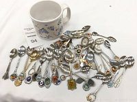 Overview of all collectible souvenir spoons arranged with the white ceramic mug.