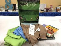 Three ladies golf shirts in pastel green, light blue, and beige laid out with golf books stacked behind them including a large hardcover book titled 'The Ultimate Golfer'.