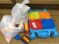 Full view of the jumbo building block table with two white bags of assorted blocks placed beside it showing the colorful top and handles.