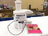 Full view of white Jack LaLanne Power Juicer with metal stand and juice recipe book next to it.