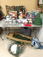 Full view of table with Christmas-related items including pillows, books, crockery, pine tree, tinsel, and ornaments.