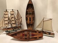 Overview of four hand carved wooden boats against white background showing two sailing ships and two smaller boats.