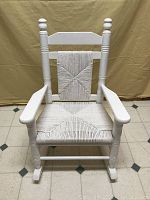 Front view of the white Cracker Barrel kid's rocking chair showing the woven seat and back with turned spindles and finials.