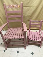 Photo showing side-by-side adult and child pink wooden rocking chairs with slatted seats and decorative backrests.