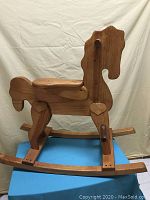 Front-side profile view of large wooden rocking horse showing saddle, peg handles, and heart-shaped leg accents