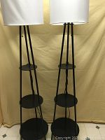Pair of black metal floor lamps with white drum shades fully visible with no items on shelves.