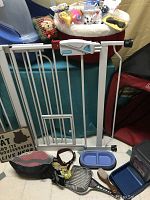 Photo showing pet gate, muzzle or harness, dog collar with leash and keys, litter scoop, brush, small decorative sign, and pet bowls