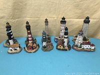 Full view of ten assorted lighthouse sculptures on a blue surface against beige background.