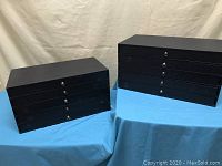 Two black jewelry cases, each with five drawers, placed on a blue cloth surface.