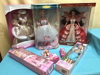 Front view of all Barbie dolls still in original packaging, showing four large boxed dolls and three smaller boxed dolls arranged on a blue fabric surface.