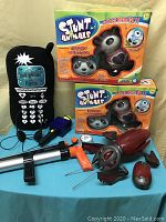 Photo shows two Stunt Animals toys in box (giraffe and panda), a stuffed cell phone radio toy with wired earbuds, a marshmallow gun, and three small red and silver themed toys resembling robotic insects/crabs or eggs.