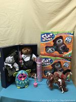 Wide view of all toys included in lot showing teddy bear, two boxed stunt animals, Furby, toy horse, and microphone.
