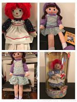 Large 36-inch Raggedy Ann doll with red yarn hair in vintage white pinafore and blue floral dress, next to a 36-inch dark-haired plush doll with blue dress and purple shirt, accompanied by a Raggedy Ann hardback book.