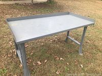 Gray metal work table on grass with raised edges on three sides and sturdy legs.