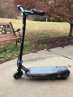 Full side view showing electric scooter with black deck, blue handlebar grips, and front wheel.