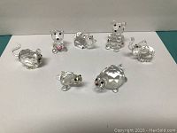 Seven clear crystal animal figurines displayed on white background: mouse, adult turtle, baby turtle, three bears, and elephant.