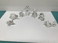 Seven clear crystal animal figurines arranged in a slight curve on a white background, including turtles, birds, dogs, bear, and a swan, showing different perspectives of each piece.