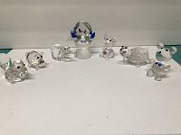 Group shot of seven crystal figurines including bird on birdbath, pig, two bears, elephant, turtle, and small mouse/koala-like figure