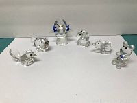 Six clear crystal animal figurines arranged against white background: mouse, bird, bird bath figure, dog, bear, and bear with blue accents.