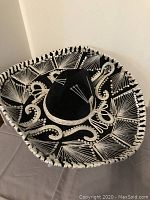 Top view of large black sombrero hat with detailed white embroidery and white braided trim around the brim.