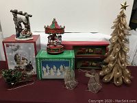 Full view of all items on a table including Nativity scenes, carousel, trains, sleigh, clear figurines and gold mesh tree