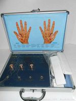 Open case showing blue hand acupoint therapy console with labeled male and female acupoint hand charts, copper electrodes, and white straps.