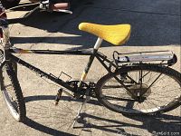 Side view of Peugeot bicycle showing black frame, yellow saddle, rear rack, and tires.