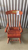 Full view of miniature wooden rocking chair with vertical spindles and curved arm rests, visible scratches on arms and seat.