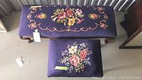 Photo showing the needlepoint upholstered bench and ottoman together, both with floral designs on purple fabric and wooden legs on the bench.