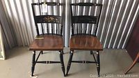 Pair of solid wood Hitchcock style chairs with floral painted backrests and natural wood seats.