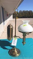 Full view of the brass lamp with white glass shade and oil reservoir on a teal surface outdoors.