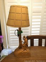 Front view of the wood chiseled lamp showing seated man figure and lamp shade.